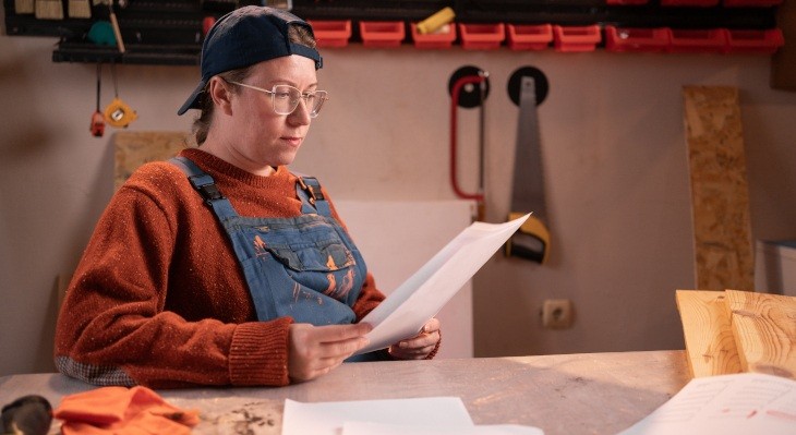 © Andrii Lysenko - Adobe Stock Frau in Werkstatt an Tisch sitzend. Sie blickt auf ein Blatt Papier.