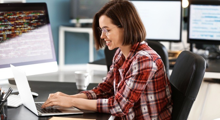 Frau lächelnd in Büro-Umgebung vor Laptop sitzend