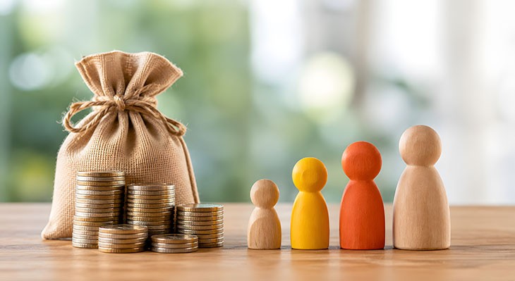 © AI Image Studio - Adobe Stock (generiert mit KI) Geldsäckchen, Münzen und Spielfiguren aus Holz auf einem Tisch